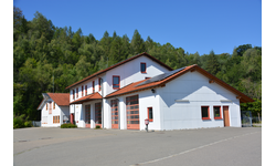 Bauhof und Feuerwehr Warthausen, ein modernes, weißes Gebäude mit roten Dächern steht vor einem bewaldeten Hügel.