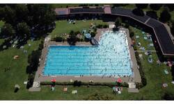 Luftbild des großen, belebten Freibads Warthausens mit vielen schwimmenden und sich entspannenden Besuchern auf umgebenden Liegewiesen.
