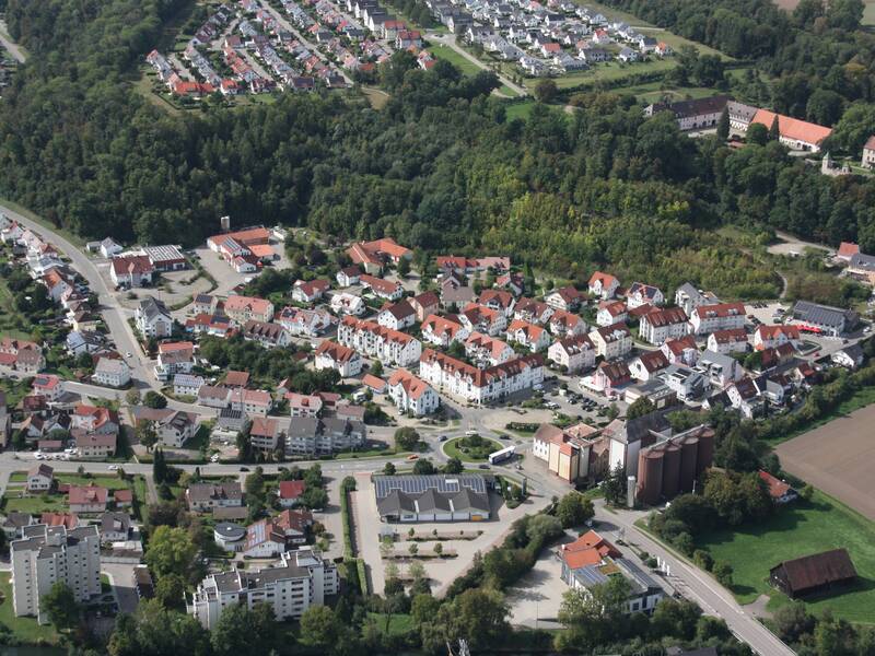 Eine Luftaufnahme zeigt Warthausen mit roten Dächern umgeben von Wäldern und Feldern.