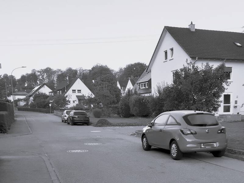 Eine ruhige Wohnstraße mit parkenden Autos und mehreren Einfamilienhäusern auf beiden Seiten.