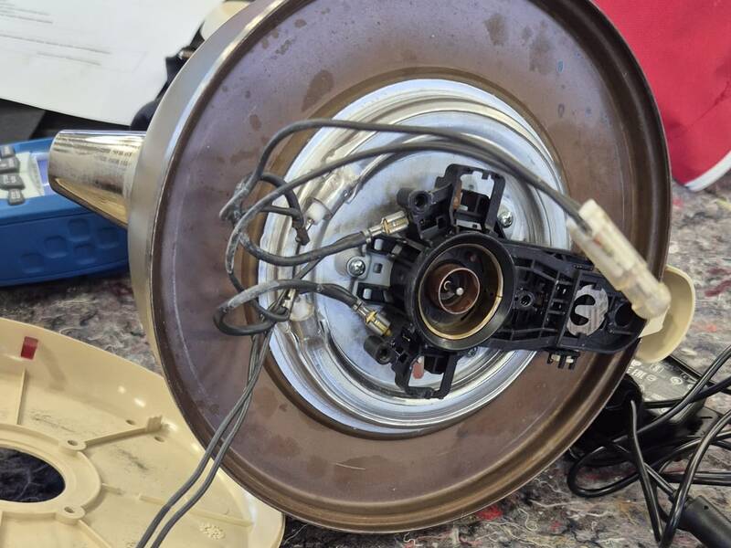 Auf einem Tisch liegt ein auseinandergebautes Haushaltsgerät mit sichtbarer Elektronik und Kabeln neben einem Laptop.