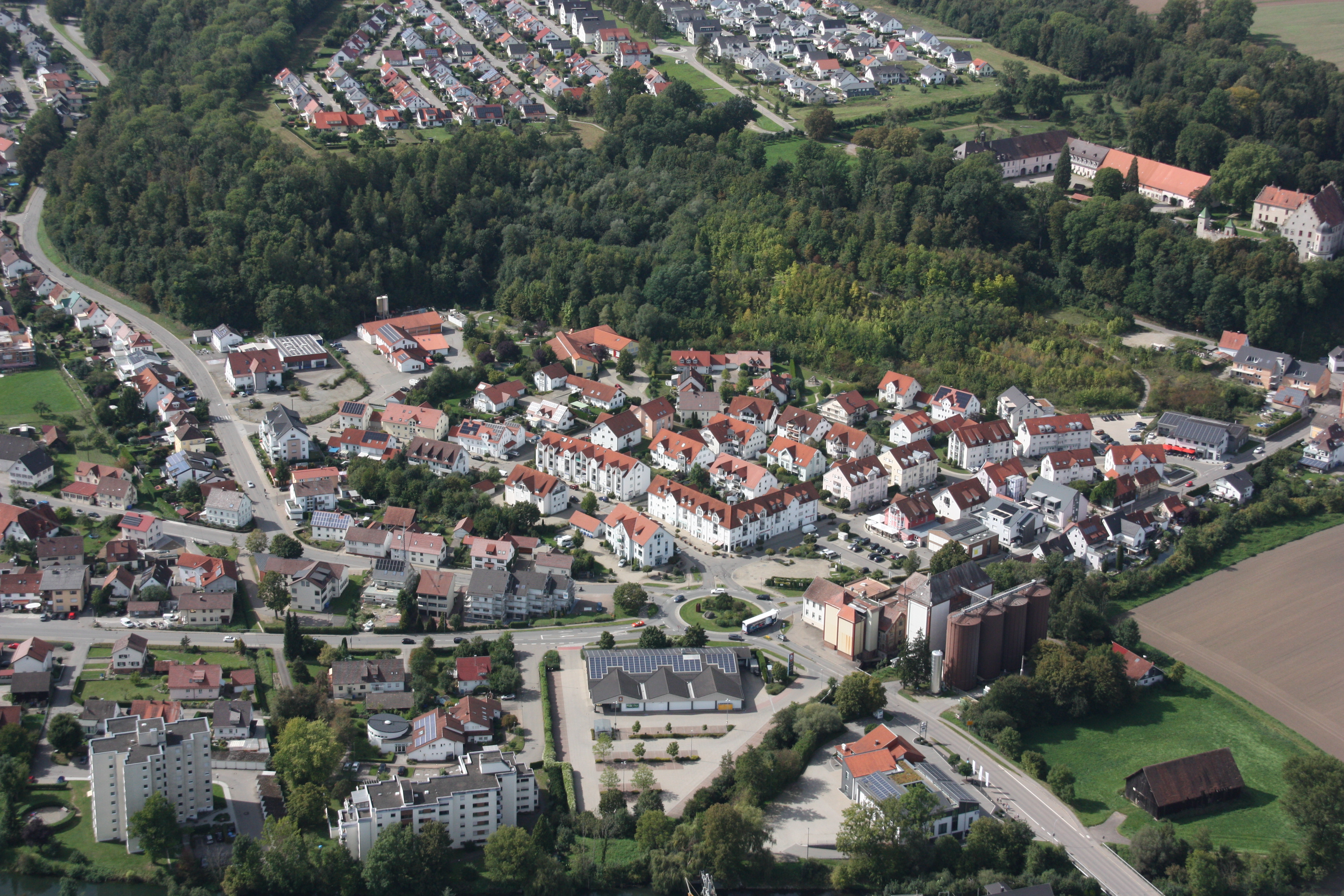 Eine Luftaufnahme zeigt Warthausen mit roten Dächern umgeben von Wäldern und Feldern.